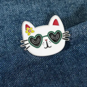 Detail of a white cat enamel pin wearing heart sunglasses on blue denim fabric