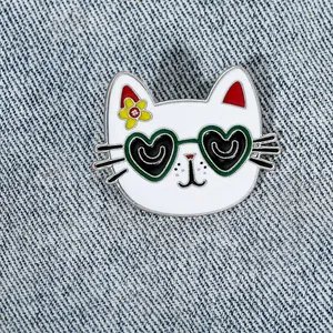 Cute white cartoon cat enamel pin with green heart sunglasses on denim fabric