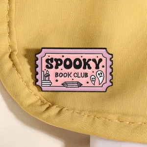 Détail du pin's émaillé Spooky Book Club rose sur fond de tissu jaune chaud