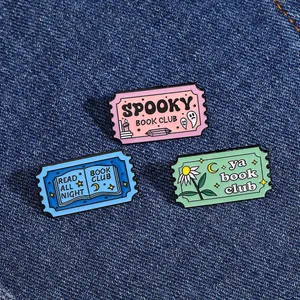 Détail de trois badges en émail coloré avec motifs Book Club sur un fond en denim bleu