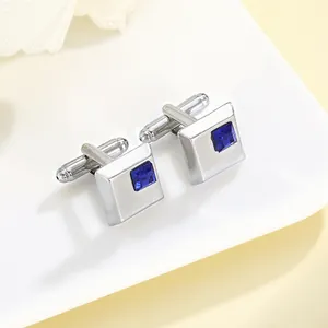 Close-up of square silver cufflinks with blue crystal inlay on a ceramic tray