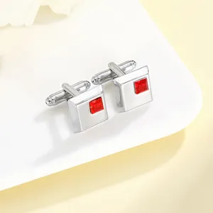 Close-up of square silver cufflinks with vibrant red crystal inlay on white ceramic plate