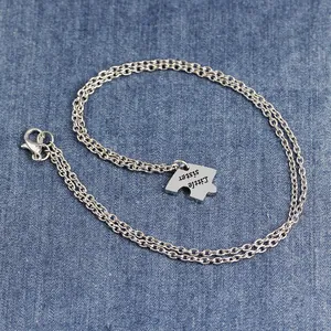 Detail of silver puzzle necklace with Little sister engraving on denim background