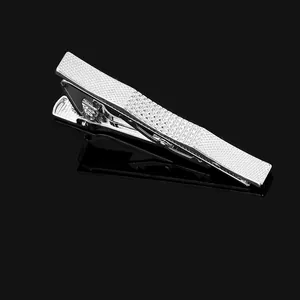 Detail of silver business tie clip with grid texture and spring mechanism on black background