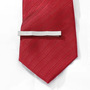 Close-up of a silver business tie clip with geometric stripes on a red striped silk tie