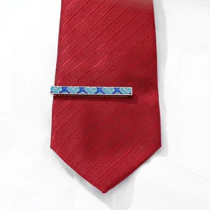 Detail of silver business tie clip with blue clover patterns on a red diagonal tie