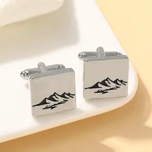 Macro detail of square silver cufflinks featuring minimalist black mountain landscape design