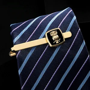 Detalle de un pasador de corbata dorado con relieve de búho en corbata a rayas