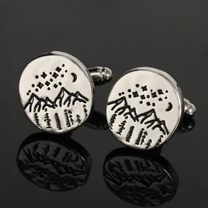 Detailed close-up of silver sun and mountain engraved cufflinks on black reflection