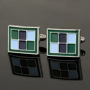 Detailopname van vierkante metalen manchetknopen met blauw en groen emaille geometrisch patroon