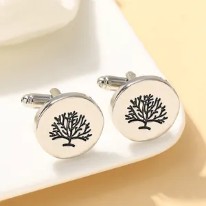 Detailed close-up of round silver cufflinks with black etched tree pattern on white tray