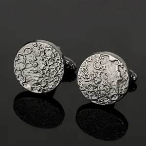 Detailed close-up of silver-tone round cufflinks with textured moon surface design