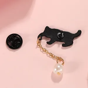 Broche chat en émail noir avec chaîne dorée et perle sur un fond rose élégant