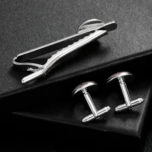 Polished silver necktie clip and cufflinks set for men on black leather background