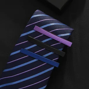 Close-up of matte metal tie clips in purple, black, and blue on a striped business tie