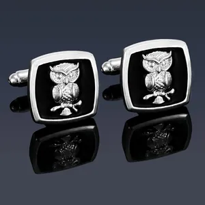 Macro detail of silver owl cufflinks with black enamel on a reflective surface