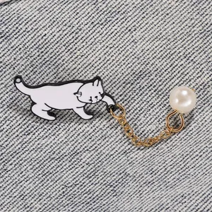 Détail d'une broche chat en émail blanc avec pendentif perle sur tissu denim
