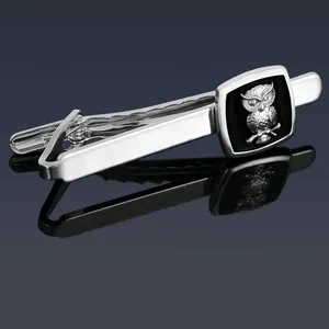 Close-up of silver owl tie clip with black square inlay on blue reflective background