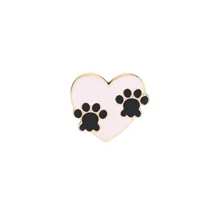 Detailed close-up of pink heart enamel brooch with black paw prints and gold alloy trim