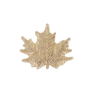 Elegant gold maple leaf brooch with textured dot pattern on a white background
