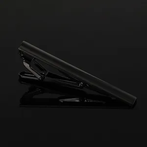Detailed view of a sleek black metal necktie clip on a reflective dark mirror surface