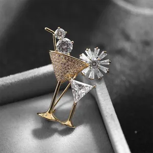 Close-up of golden cocktail glass brooch with sparkling white zircons on grey velvet base