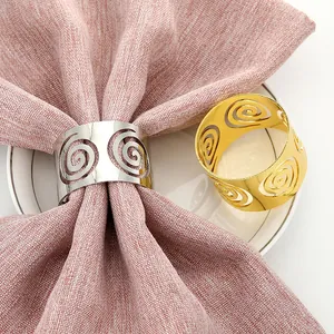 Golden and silver alloy hollow spiral napkin rings displayed on pink linen and white plate