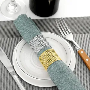 Detail of gold and silver hollow mesh napkin rings on dark teal fabric over a dinner plate