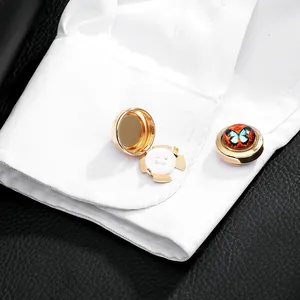 Detail of gold clip-on cufflinks with blue butterfly design on a white shirt cuff