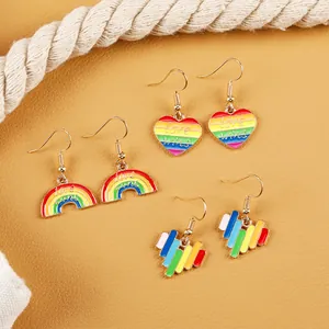Detailed macro of Love Wins rainbow heart and bridge earrings on a textured backdrop