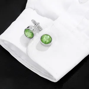 Close-up of polished silver cufflinks with emerald green crystals on white shirt cuff