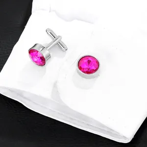 Detail of rose pink crystal cufflinks on a white shirt sleeve over a black leather background
