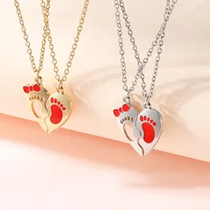 Detail of interlocking heart pendants with red footprints and bow on matching chains