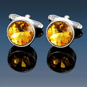 Close-up of men's silver cufflinks with faceted yellow crystal stones on reflective surface
