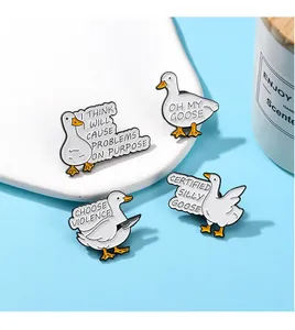 Detailed view of four funny white goose enamel pins with humorous English text on a tray