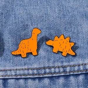 Set di due spille dinosauro arancioni a forma di nugget di pollo su sfondo di denim