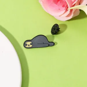 Détail d'un pin's en émail paresseux gris endormi sur un fond vert pastel frais