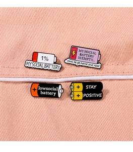 Macro view of four social battery enamel pins on pink denim fabric with smooth lighting