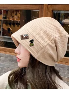 Detailed view of beige knitted beanie with ROME colosseum and black cat enamel pins