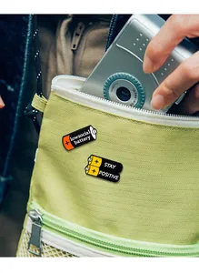 Detail of battery enamel pins with funny quotes on a light green nylon fabric bag