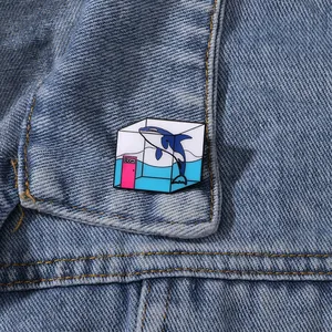 Detail of creative whale enamel pin with blue liquid container pinned on denim fabric