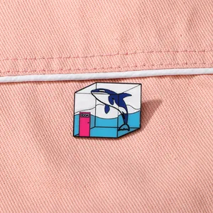 Creative cartoon killer whale enamel pin in a glass tank displayed on pink fabric