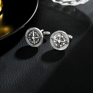 Detailed close-up of retro silver compass cufflinks on a black leather texture background