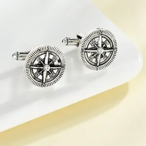 Detailed close-up of retro silver compass cufflinks with central crystal on white plate