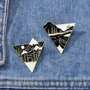 Detailed close-up of triangular enamel pins with mountain and forest scenes on denim fabric