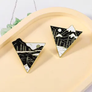 Close-up of triangle enamel pins with mountain and forest scenes in black and white finish