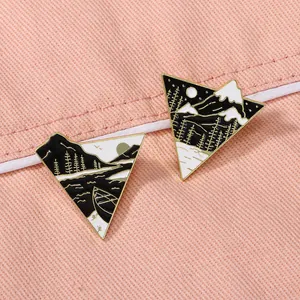 Detail of triangular enamel pins featuring mountain, lake and moon landscape illustrations