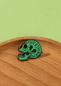 Dettaglio macro di una spilla a teschio in smalto verde con incisione Overthinking