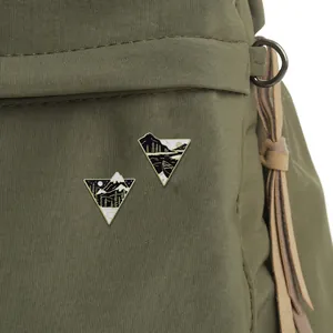 Detail of triangular nature enamel pins with mountain and lake motifs on green canvas bag