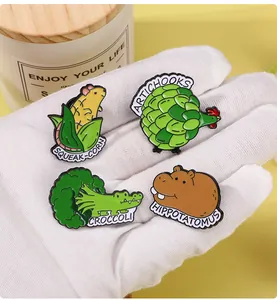 Close-up of four colorful enamel animal and vegetable badges held in hand